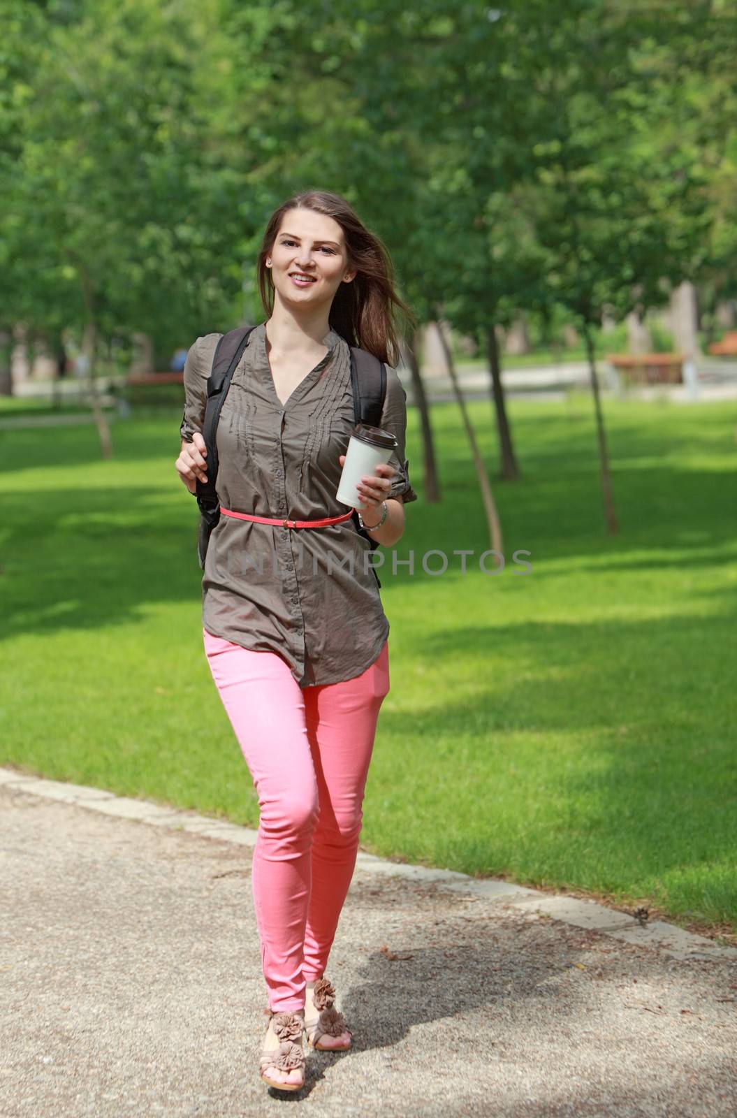Young brown hair woman with a cup of coffee in her hand running outside in a park.