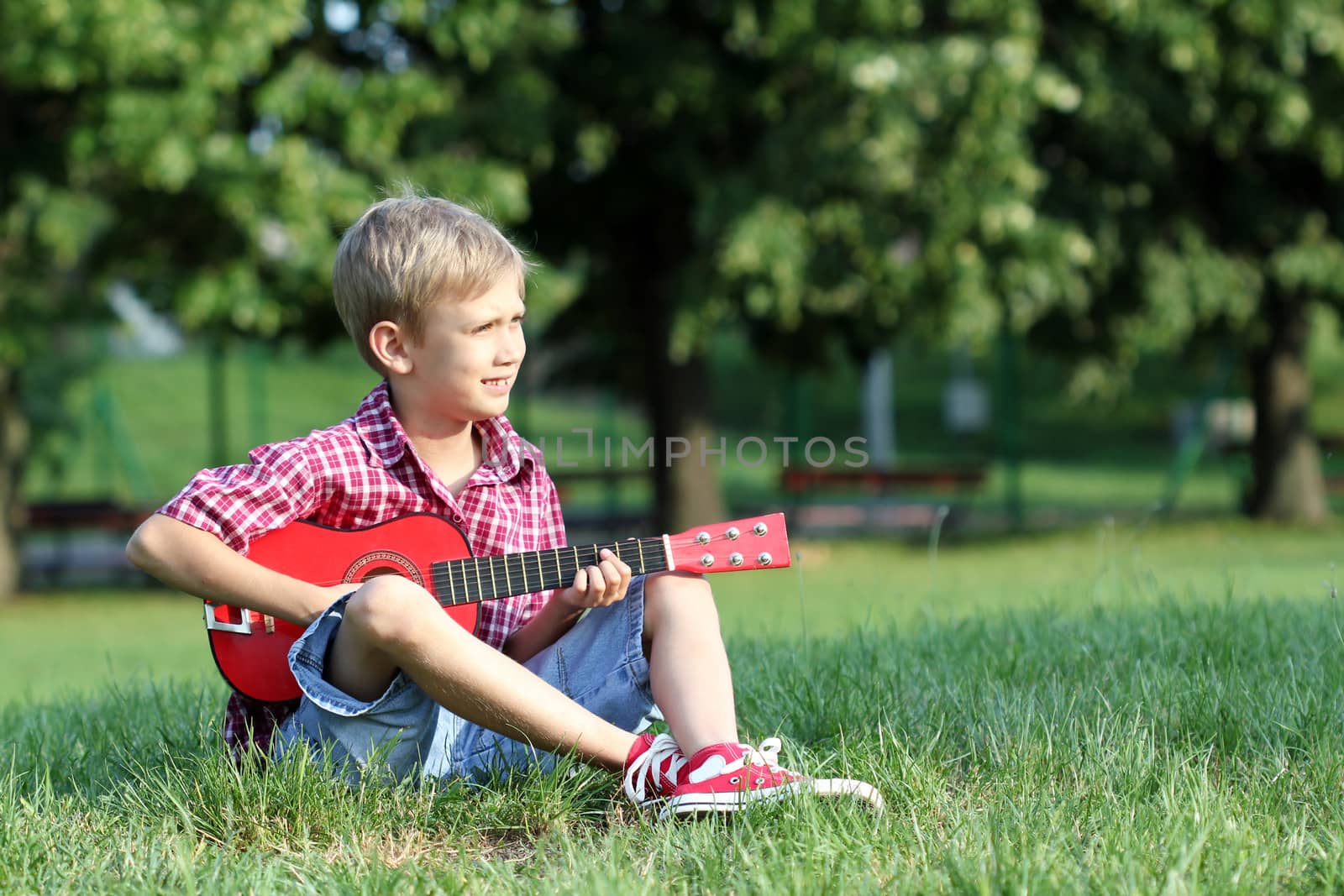 boy sitting on grass and play guitar by goce