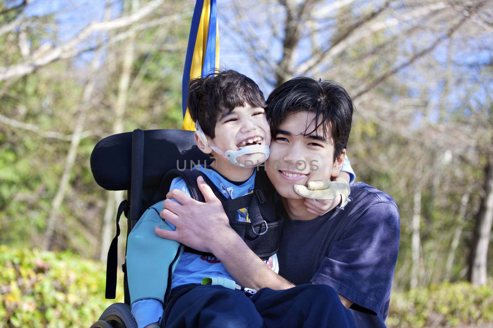 Little disabled boy in wheelchair hugging older brother outdoors by jarenwicklund