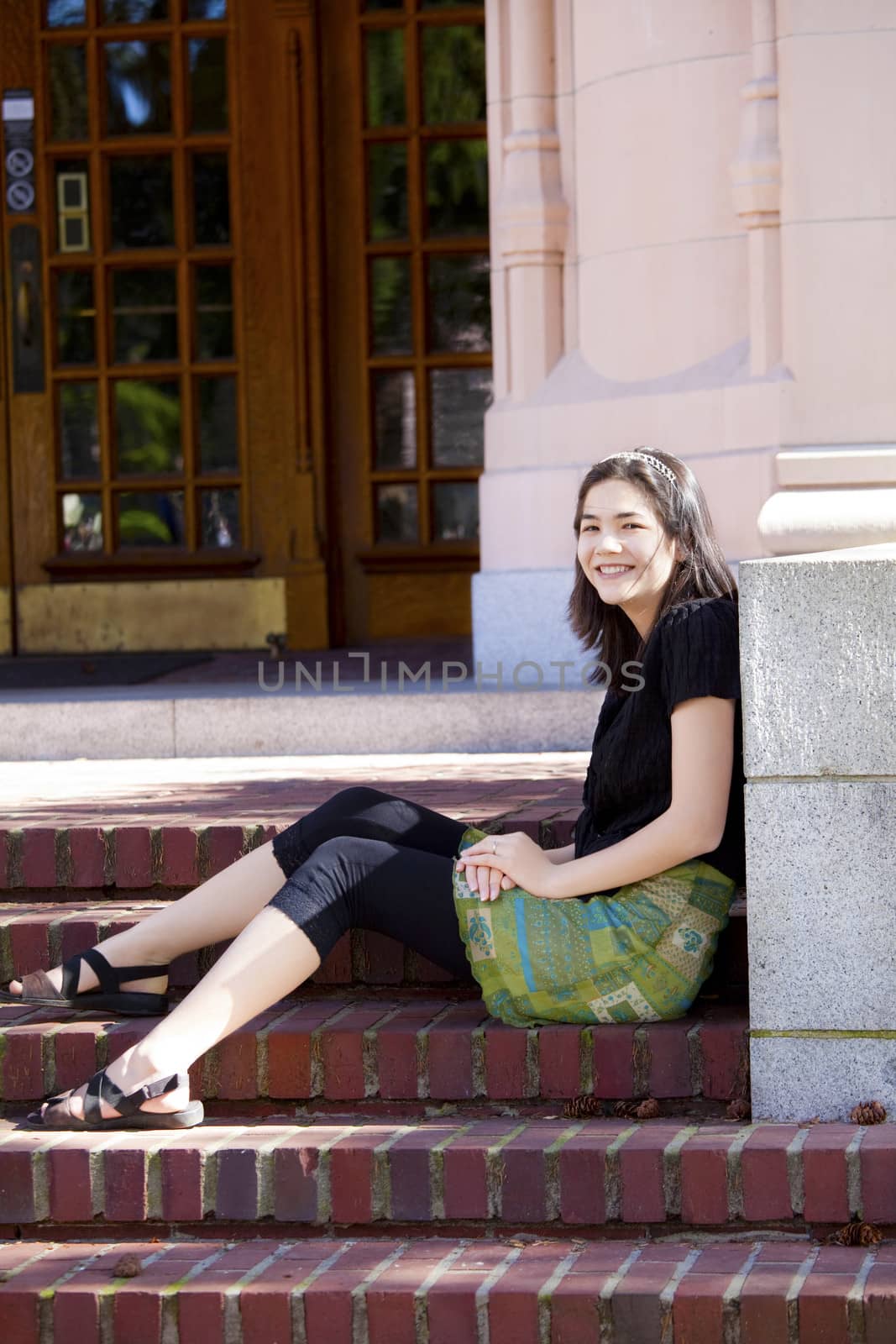 Young biracial teen girl sitting on brick steps outdoors, enjoying sunshine