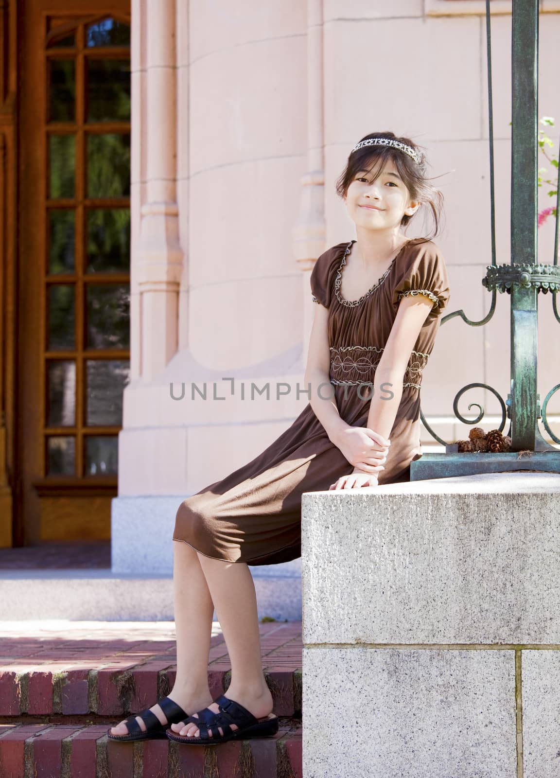 Preteen biracial girl sitting on stone wall, enjoying sunshine outdoors