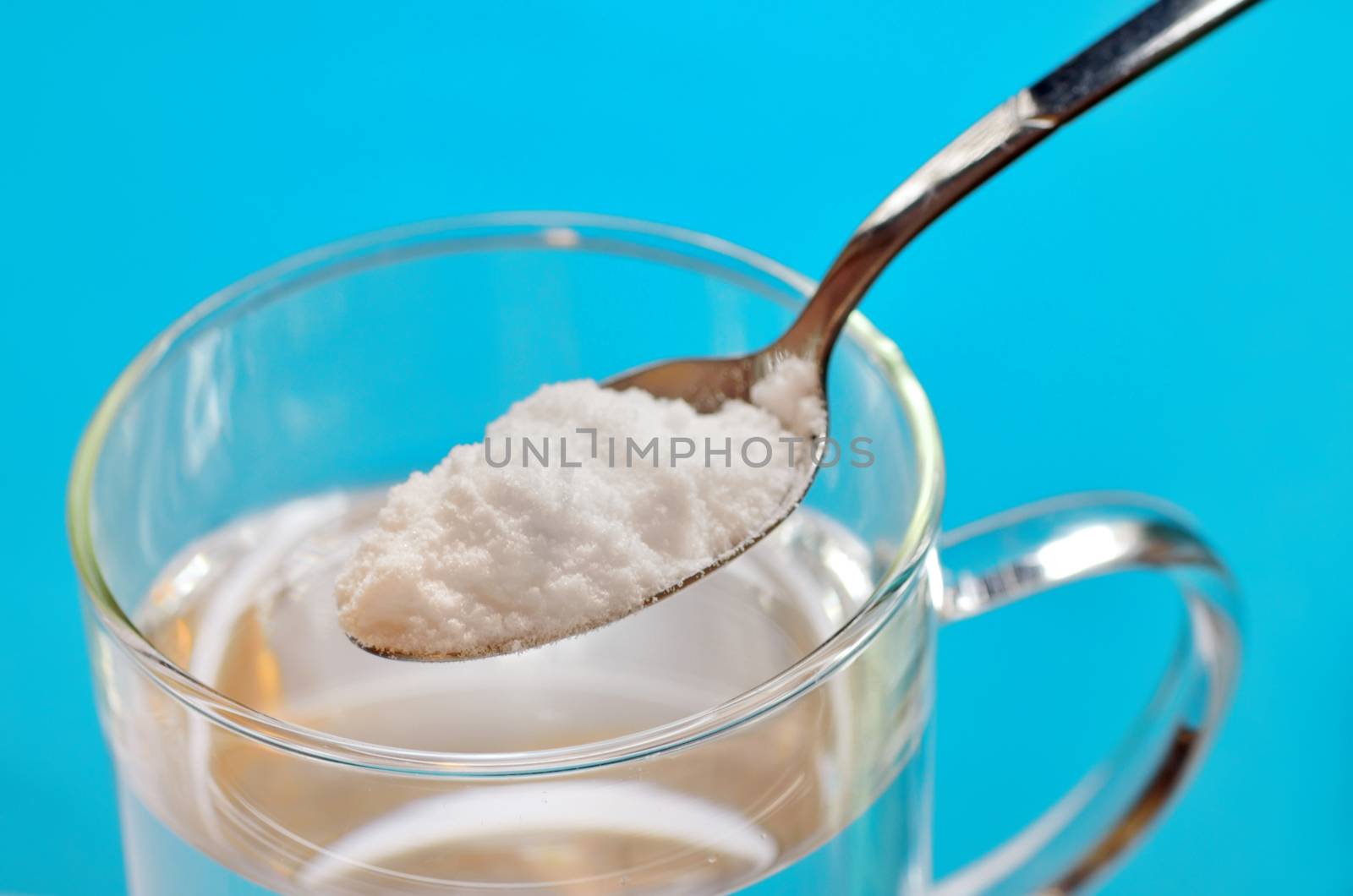 Spoon of baking soda over glass of water on blue background