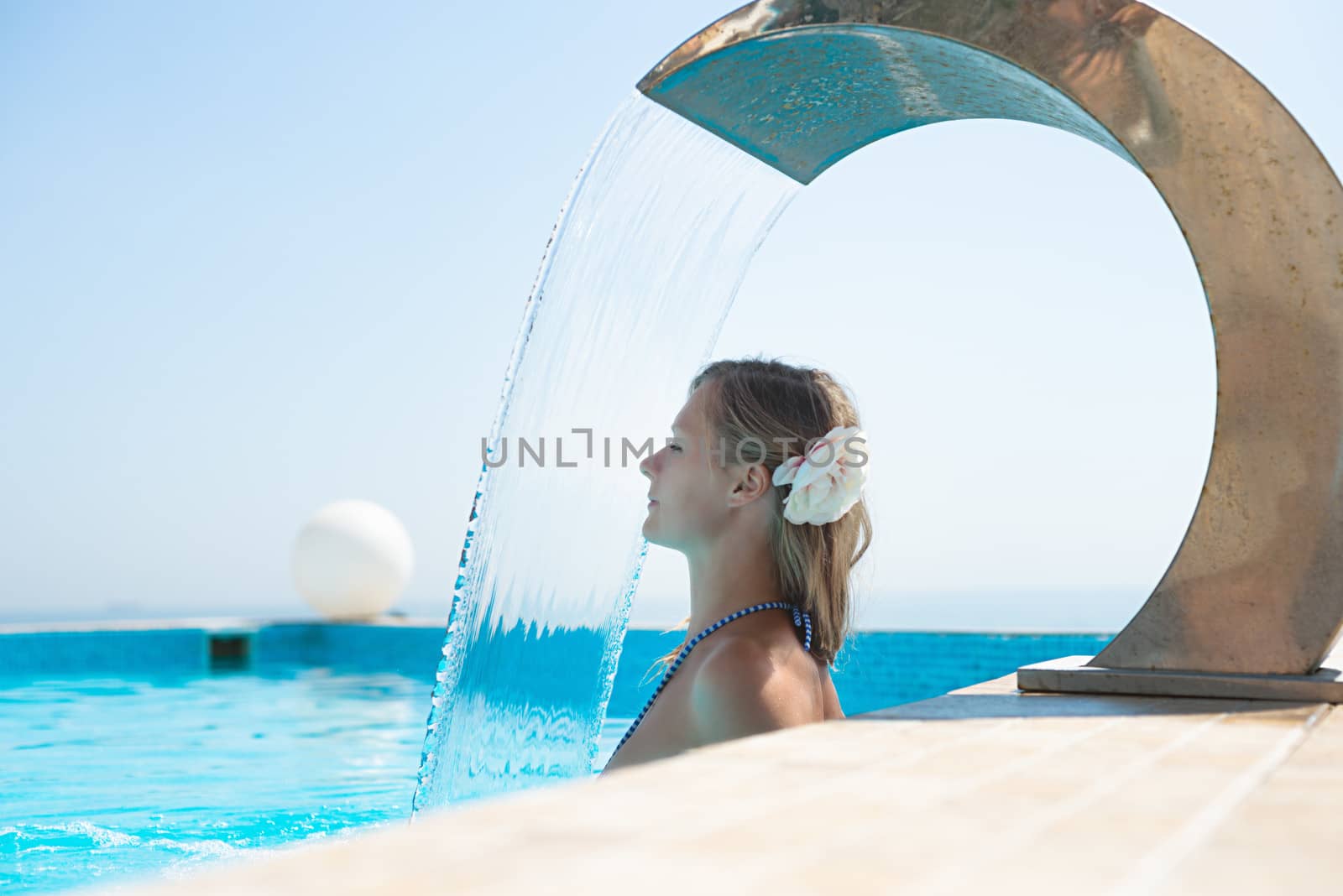 Young woman refresh in pool under the small waterfall
