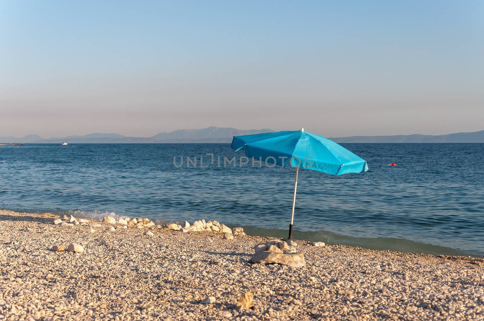 Blue umbrella on a rock beach at the sunset