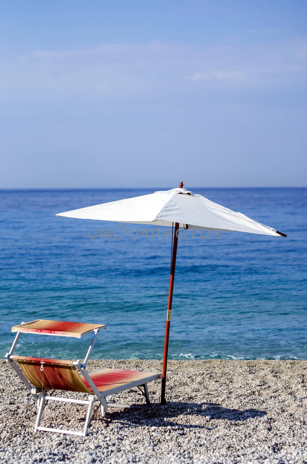 Recliner and umbrella on a pebble beach.