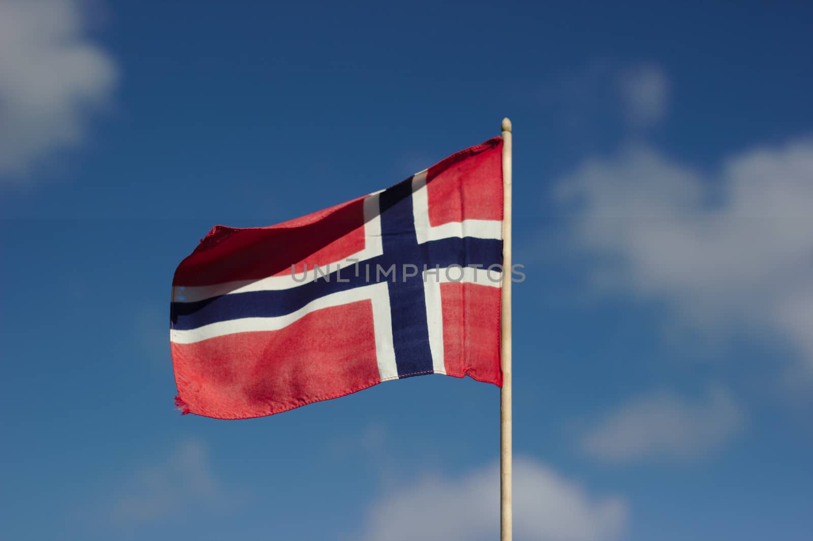 A Norwegian flag against a blue sky with white clouds.