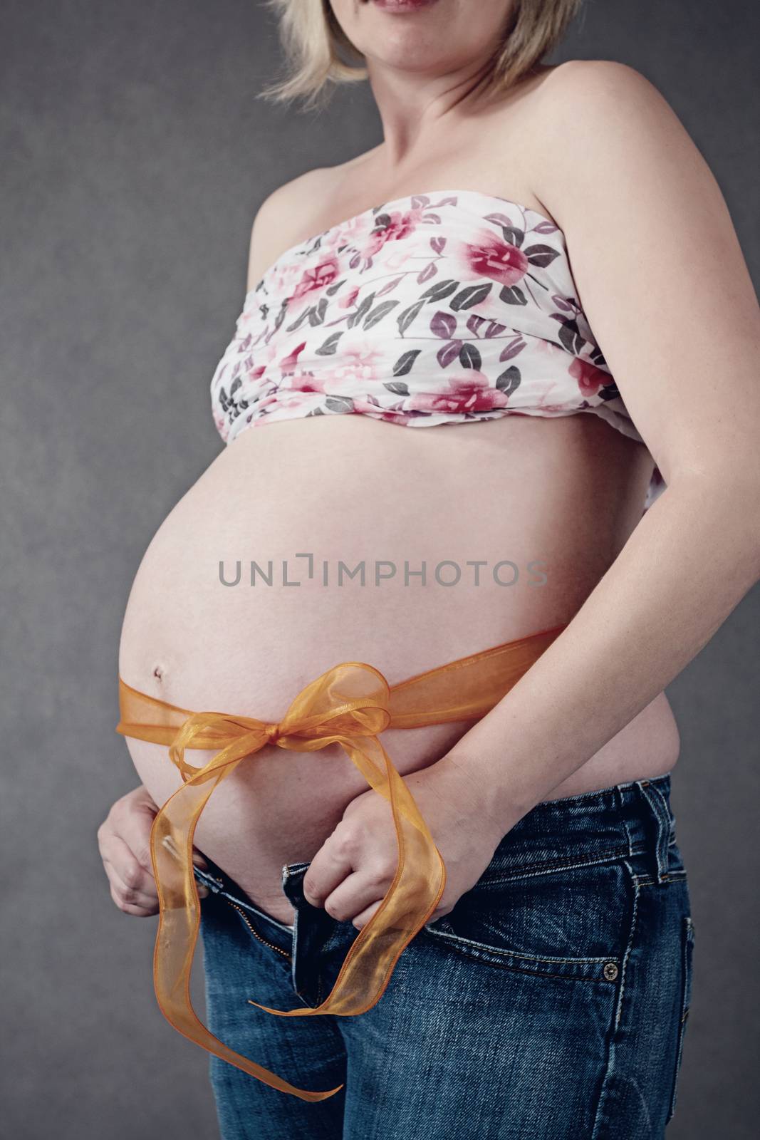 pregnant woman with ribbon around her tummy on grey background