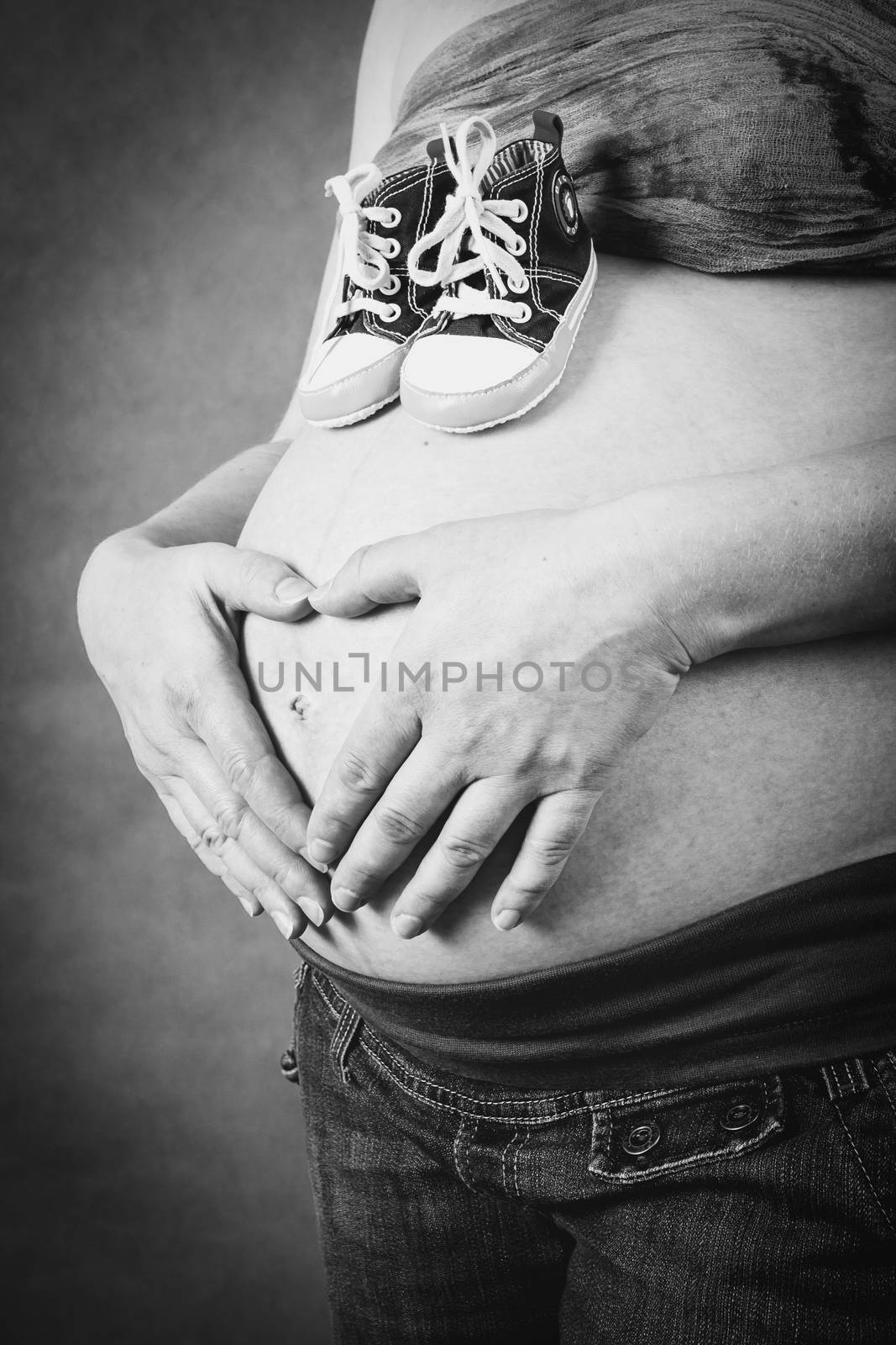 pregnant woman with a child shoe tenderly holding her tummy with hand as heart shape