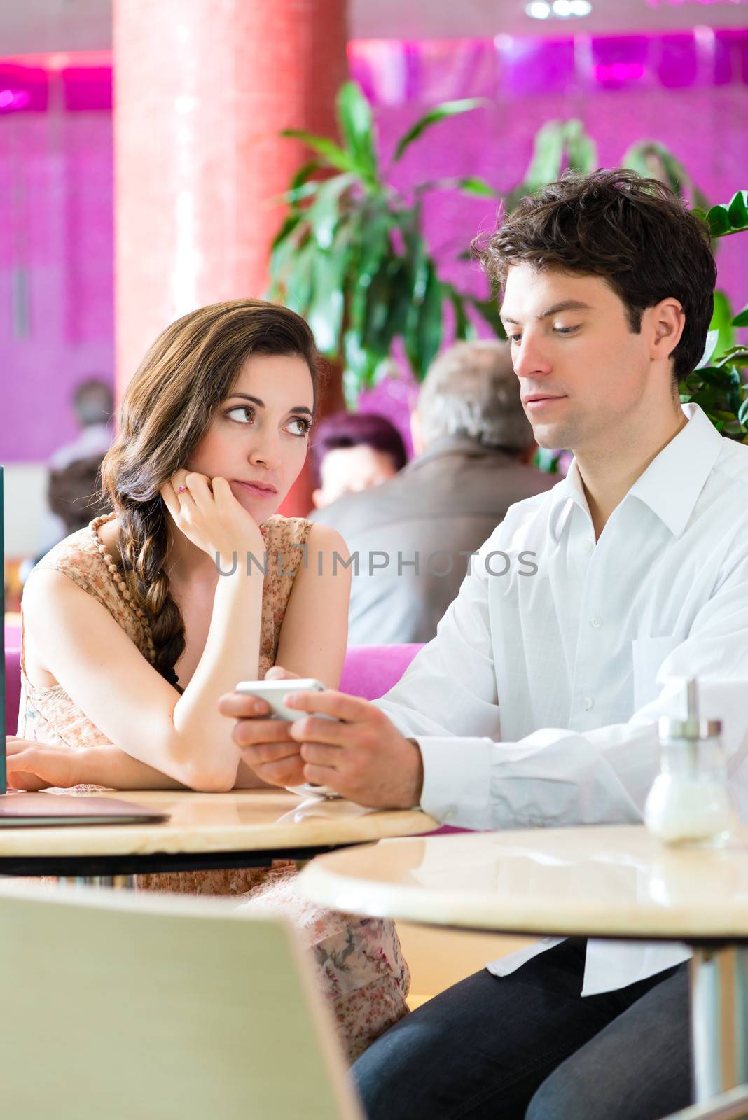 Couple in a cafe spends leisure time together, she is angry because he acts busy on the phone