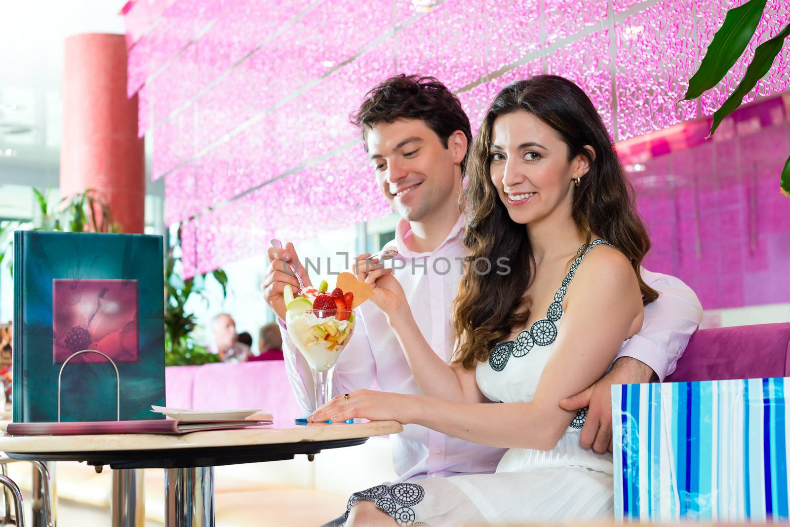 Young Couple in a Cafe eating together an ice cream sundae being happy after shopping, bags standing behind them