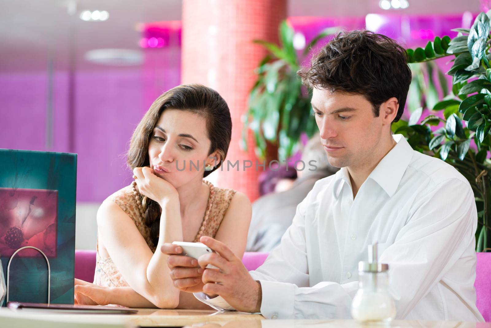 Couple in a cafe spends leisure time together, she is angry because he acts busy on the phone
