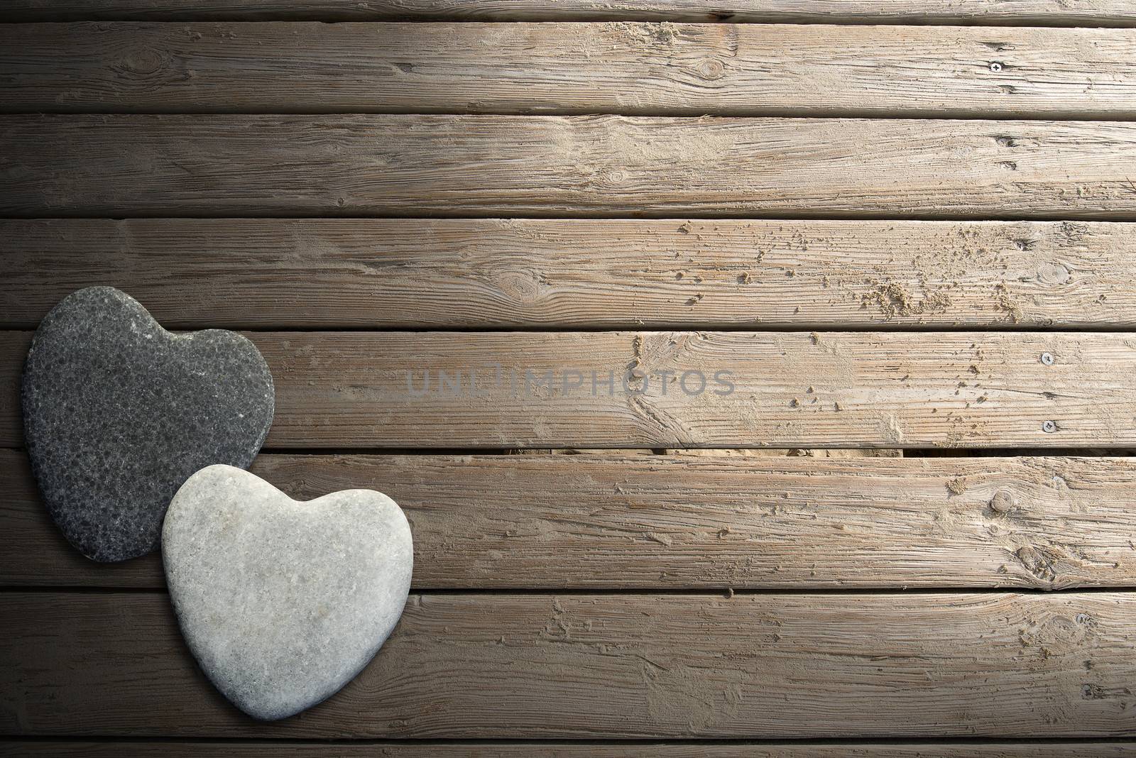 Two hearts of stone on aged beach brown wooden floor over summer sand