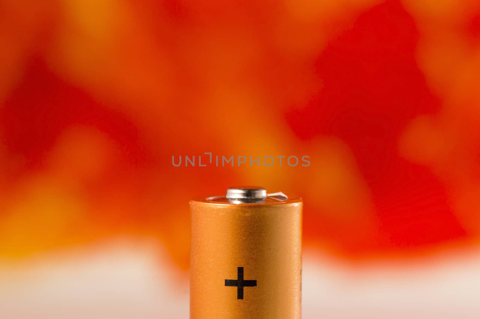 Detail of a battery with plus sign on orange background