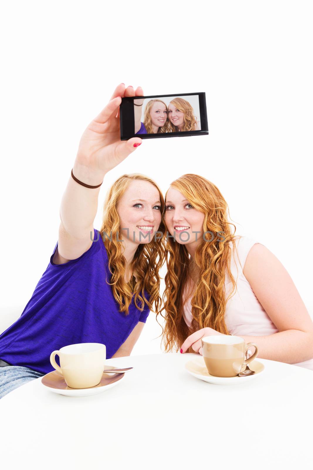 two happy women sitting at a coffee table making photos of themselves on white background