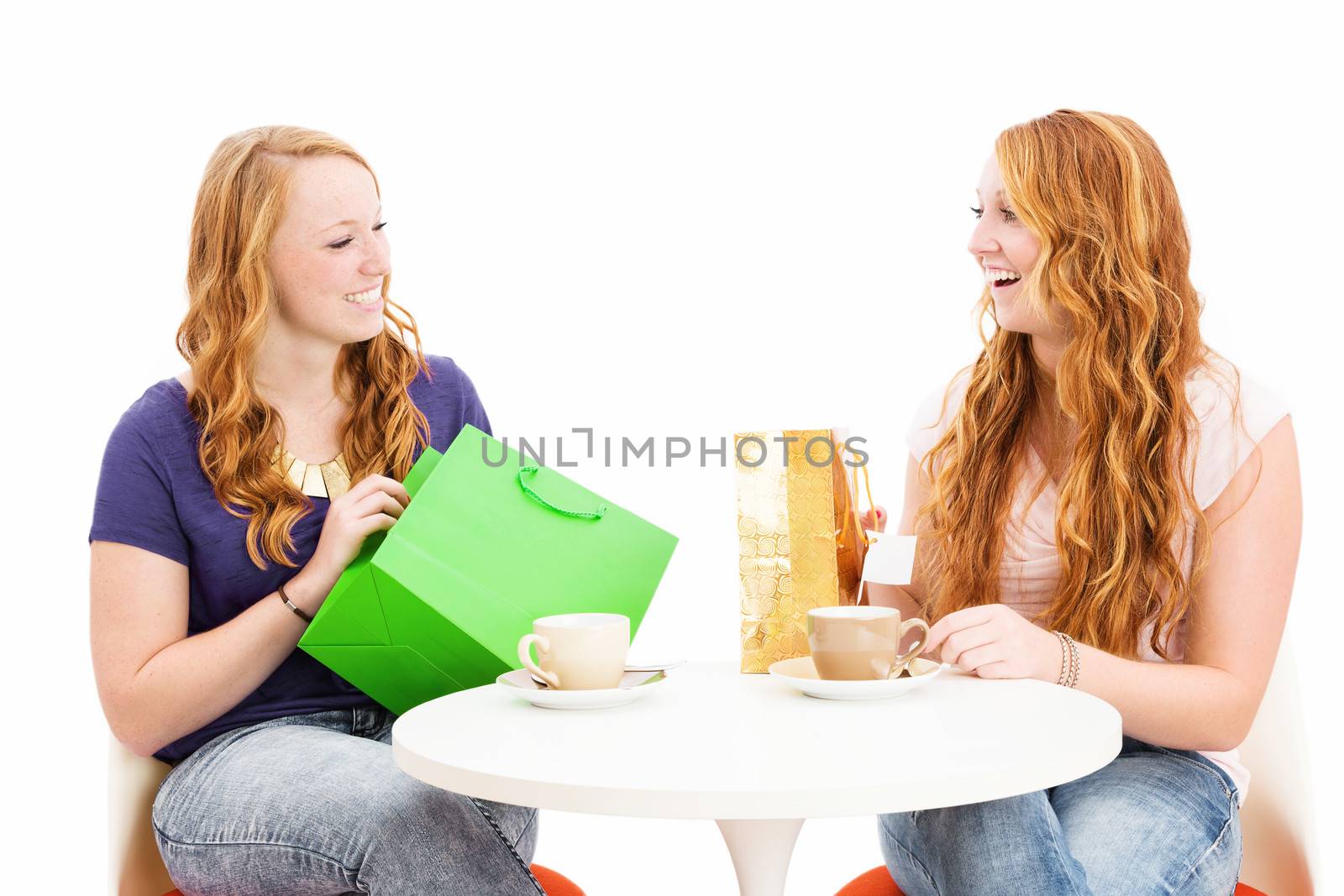 two happy redhead women sitting at a coffee table with shopping bags on white background