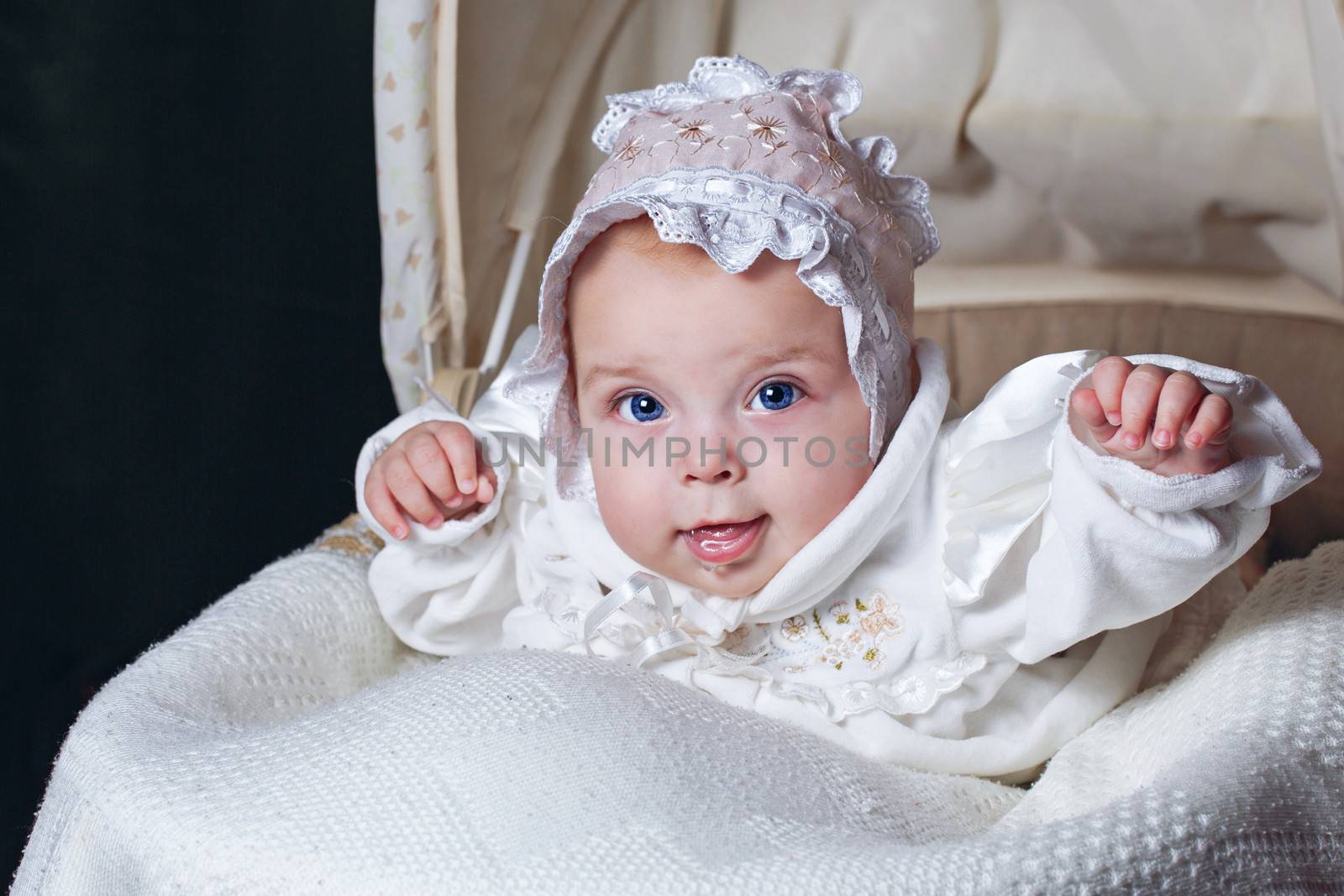 Cheerful and happy blue-eyed baby in  bonnet lies in cradle