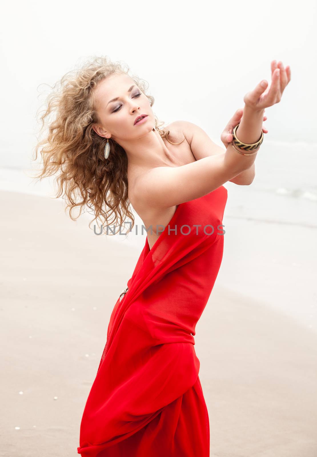Beautiful woman in red fabric posing on sea beach in foggy day