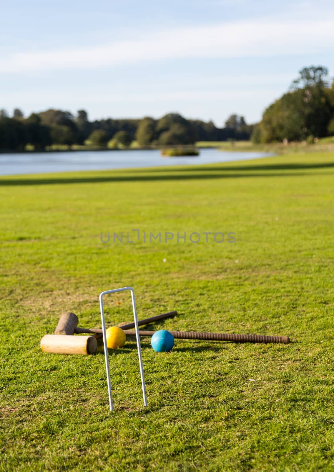 Two wooden mallets of croquet set and hoop set into green english lawn as though the game is just over