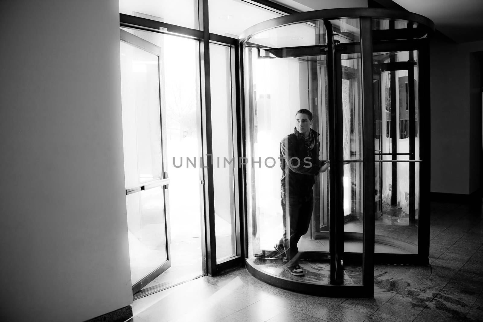 Young man in his twenties walks through a revolving doorway entrance. Black and white.