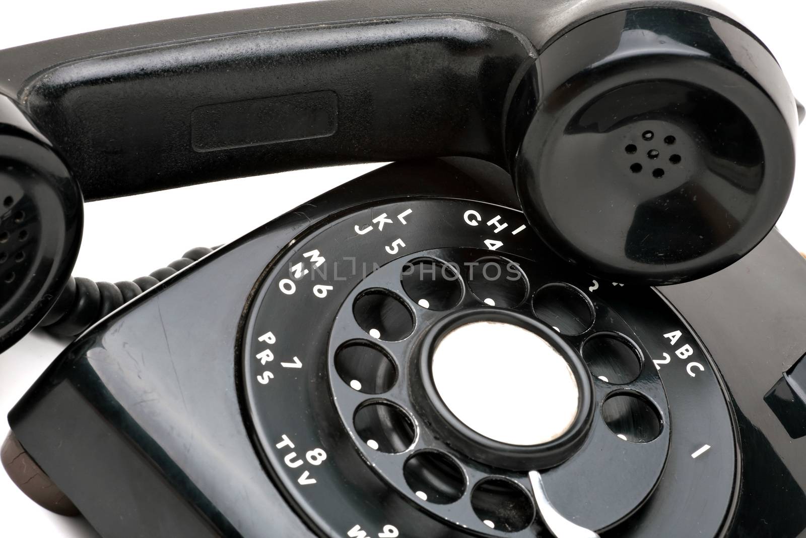 An old black vintage rotary style telephone off the hook isolated over a white background. 