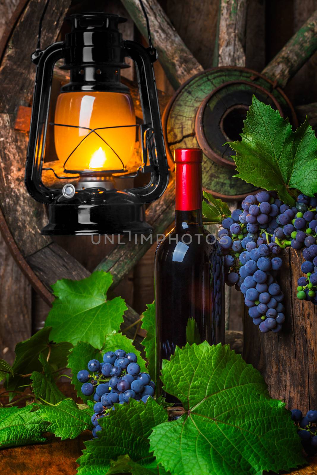 Bottle of red wine with grapes on a background of a kerosene lamp