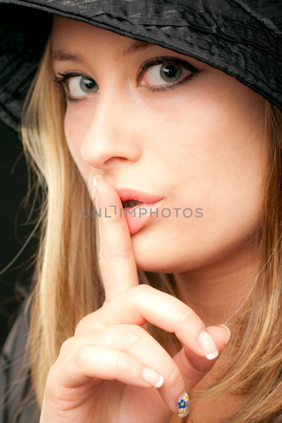 Beautiful blonde woman face showing shush with finger over mouth, looking at camera