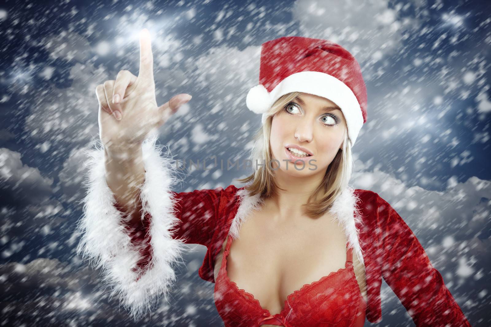 Sexy lady in revealed Santa costume with red brassiere touching stars on the sky during Christmas snowstorm