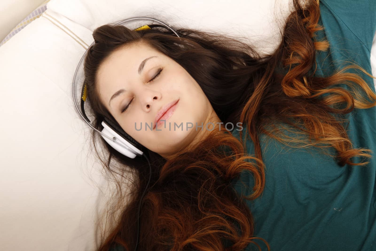 A young adult woman listening music with headphones in bed.