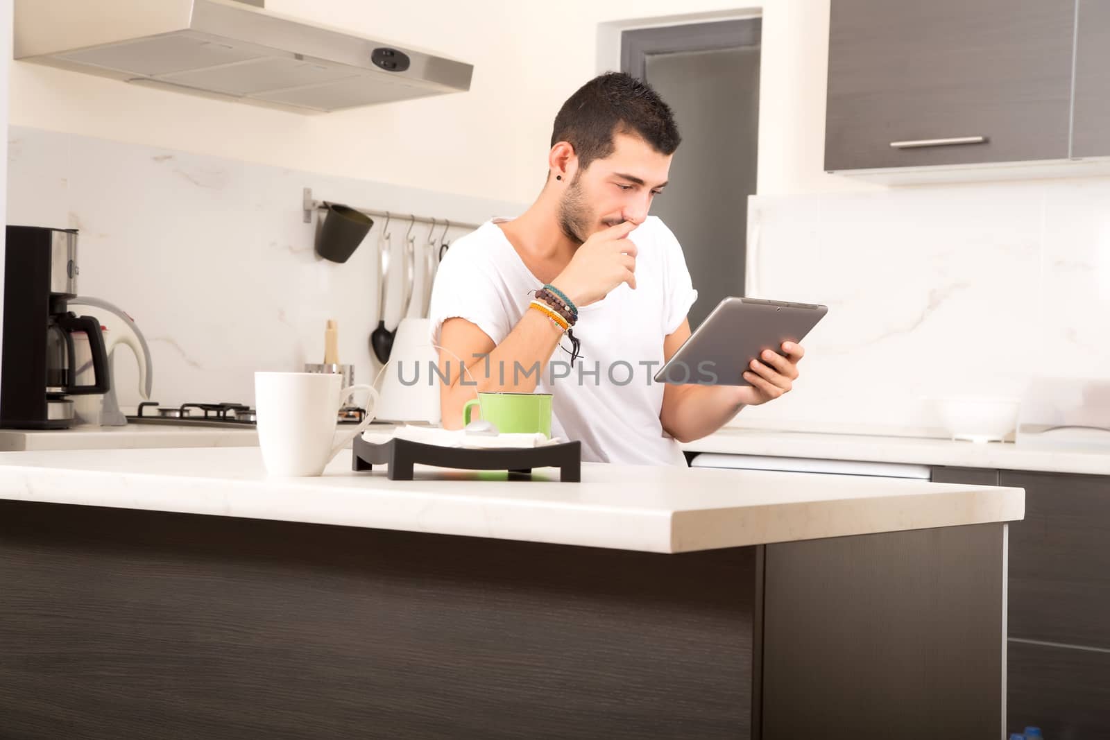 A young male sitting in the kitchen with a Tablet PC.