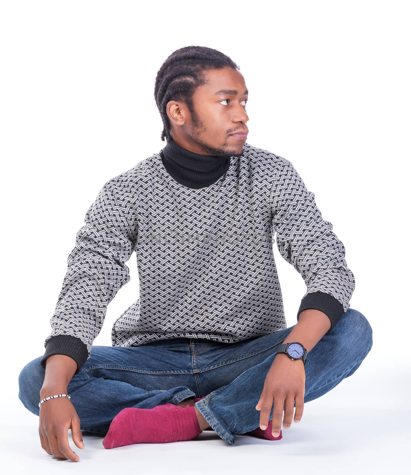 Young African-American male sitting on the ground looking to his side in a white background