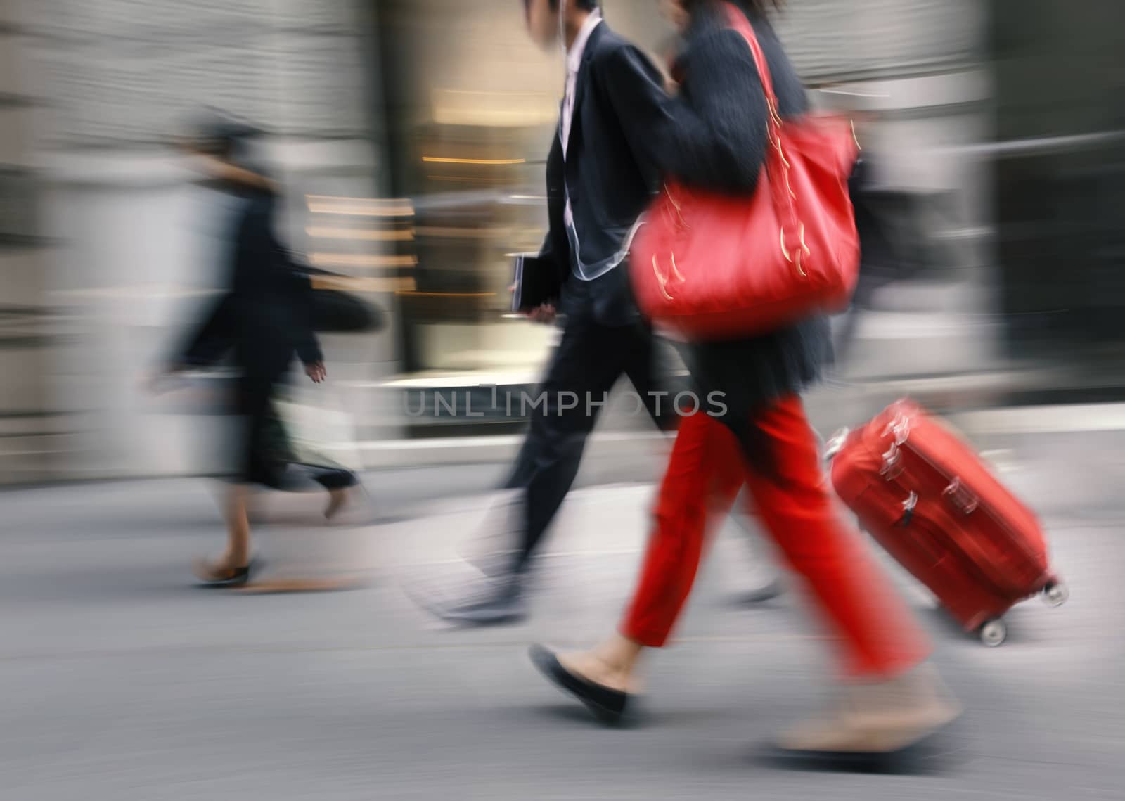 People with a red bag and a suitcase walking down the street. Intentional motion blur