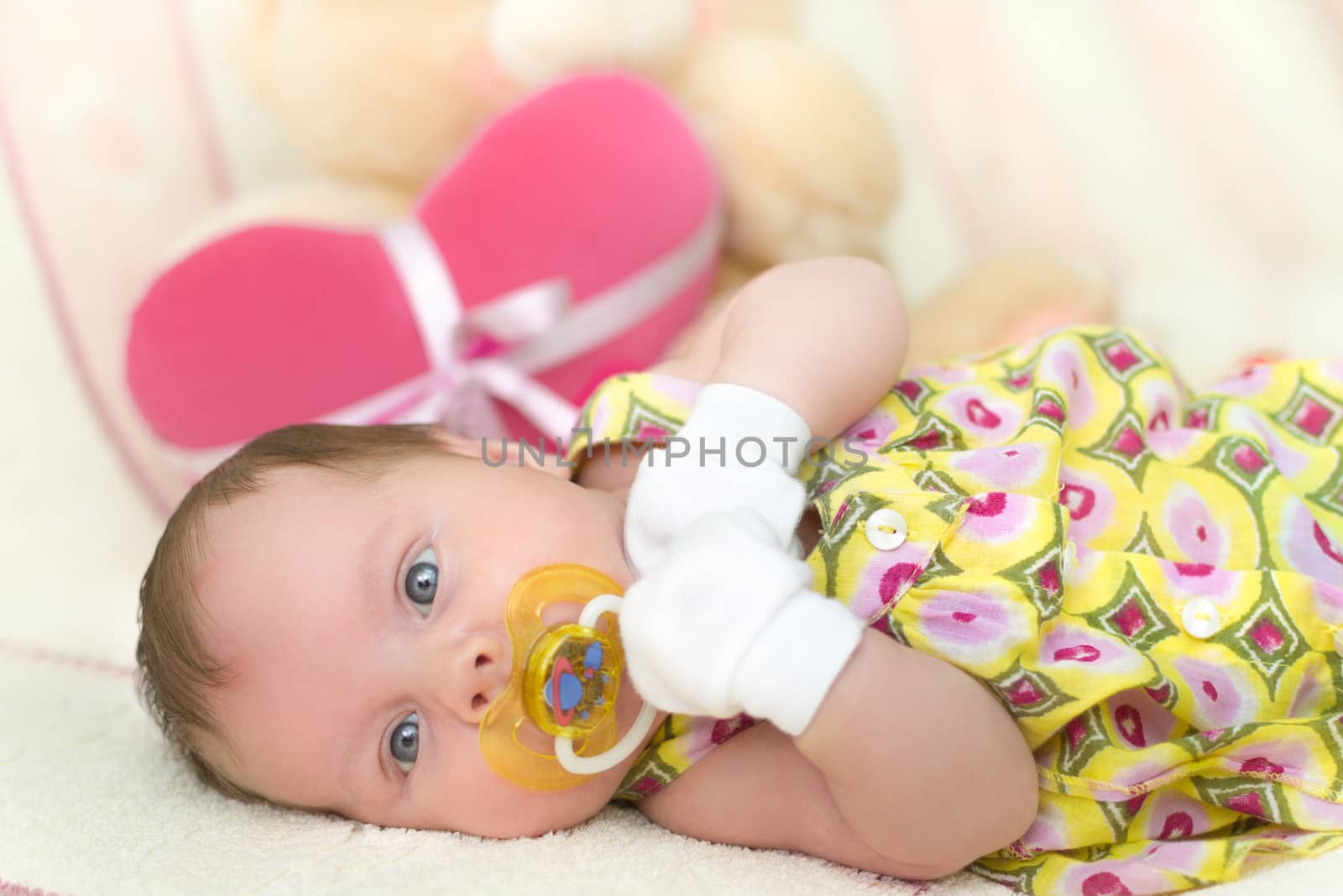 Infant baby girl (1 month old) lying on bed with teddy bear