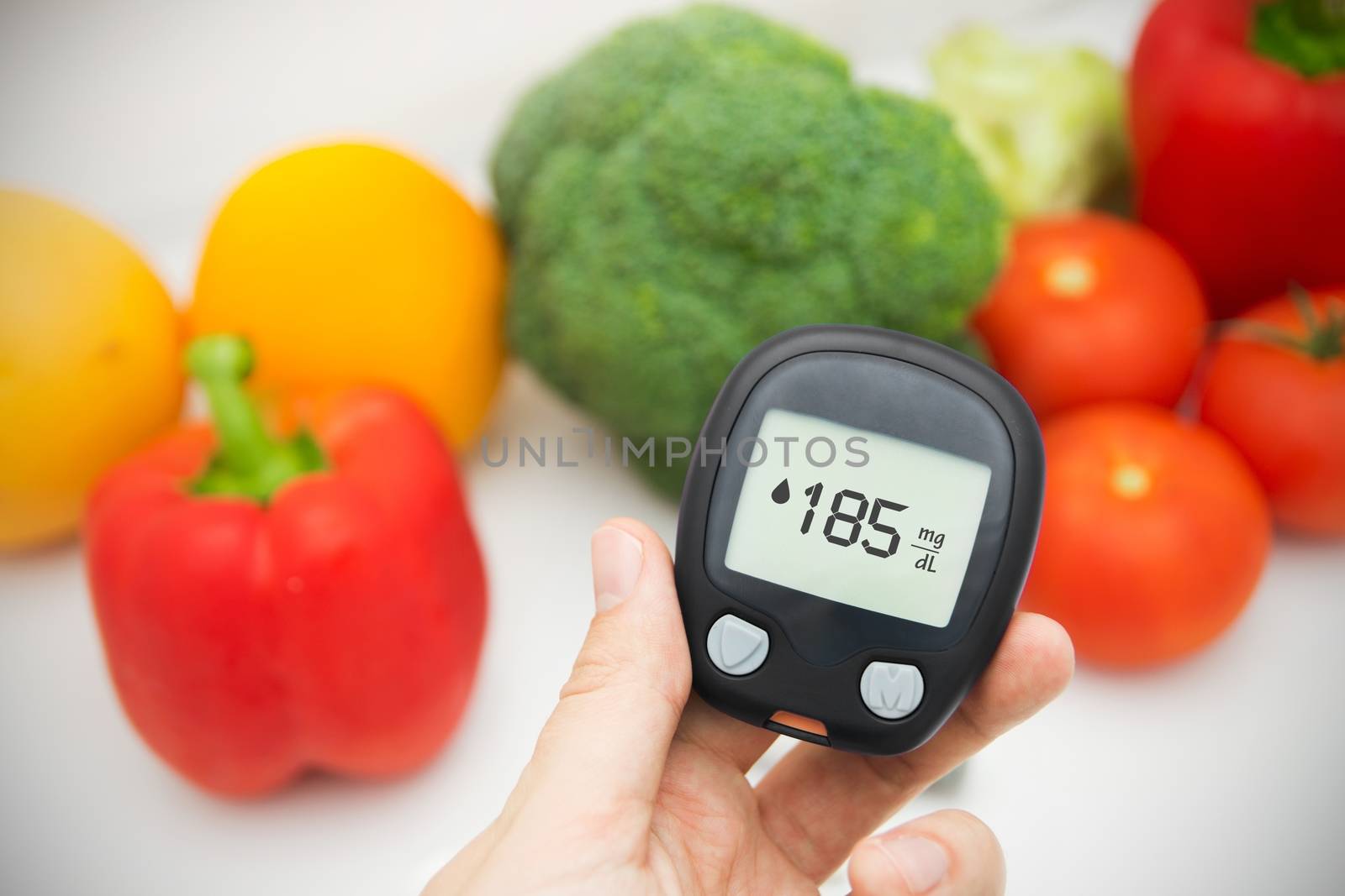 Hand holding meter. Diabetes doing glucose level test. Vegetables in background