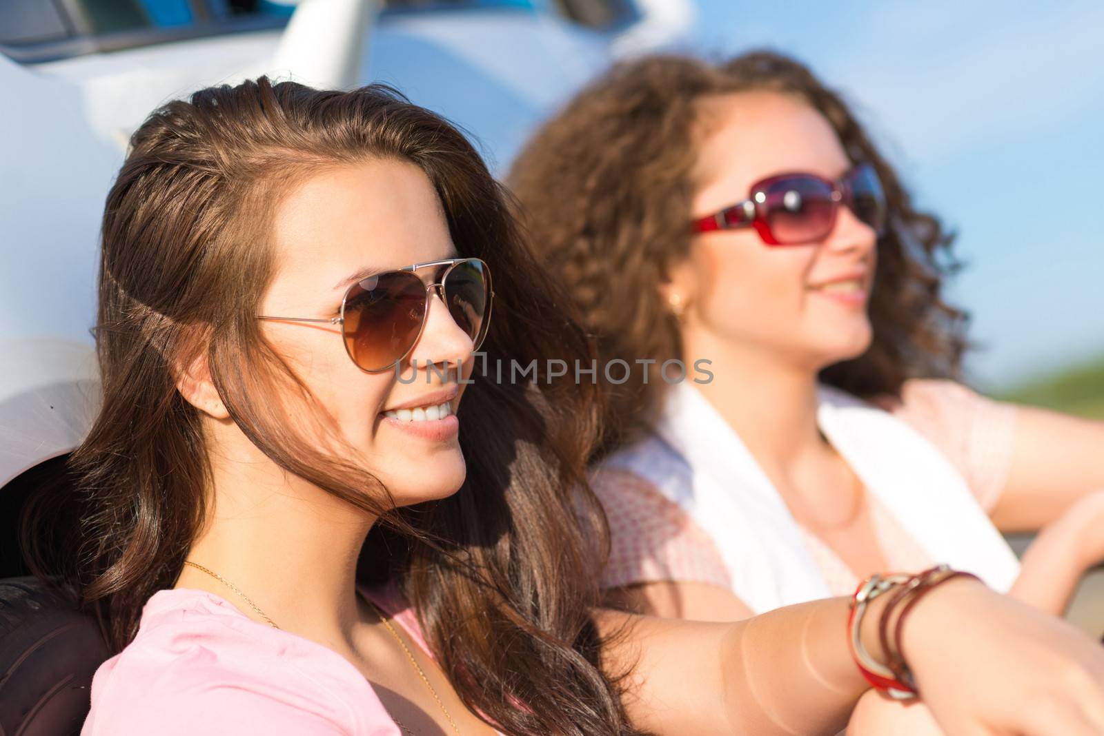 Two attractive young women wearing sunglasses, sitting next to the car