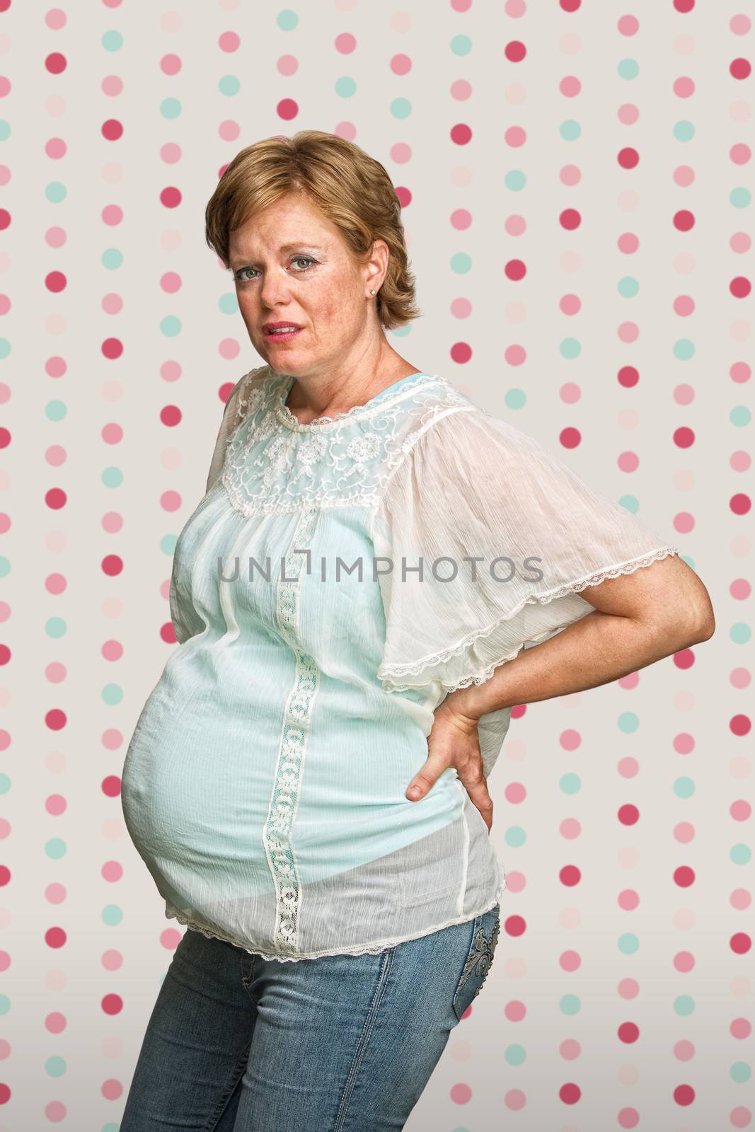 Pregnant lady holding back on polka dot background