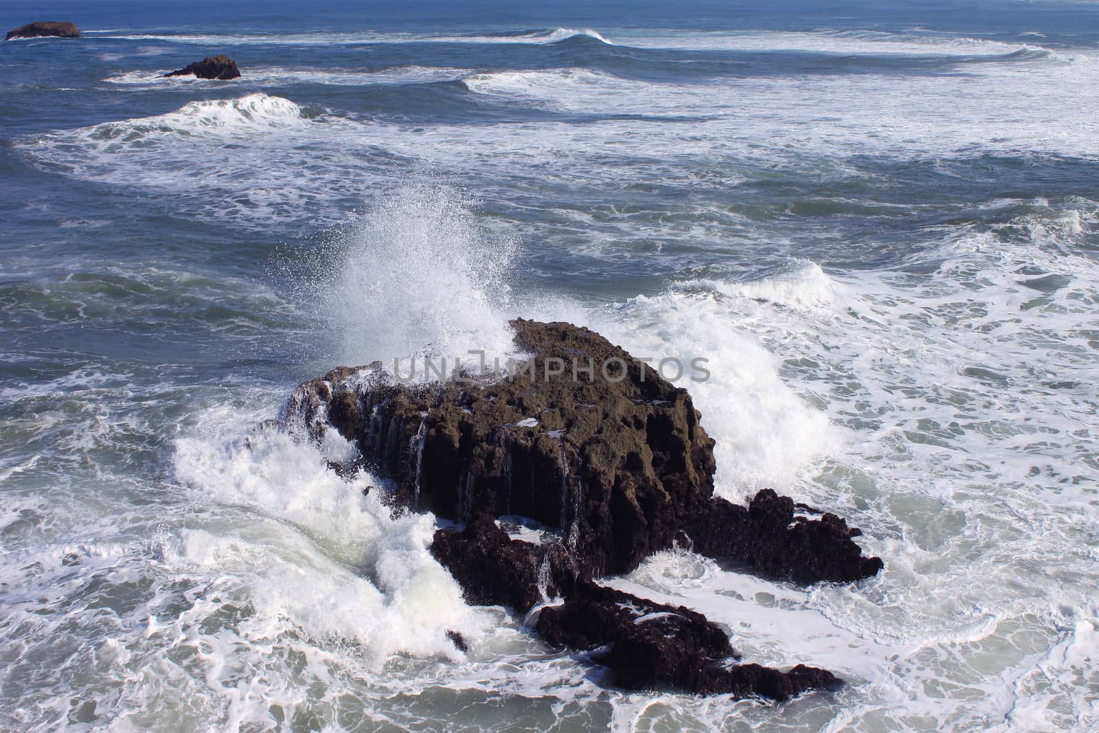 several waves at high tide break on a rock in the middle of ocean