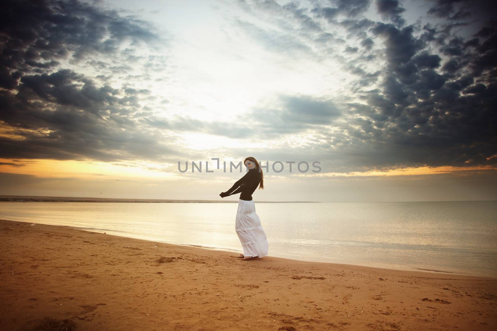 Single lady standing and walking along the beach during sunrise or sunset. Vivid colors