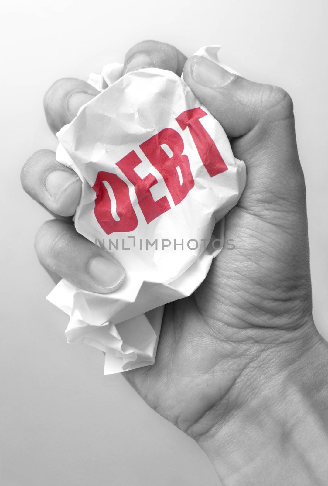 Hand squeezing a crumpled piece of paper with the word debt 
