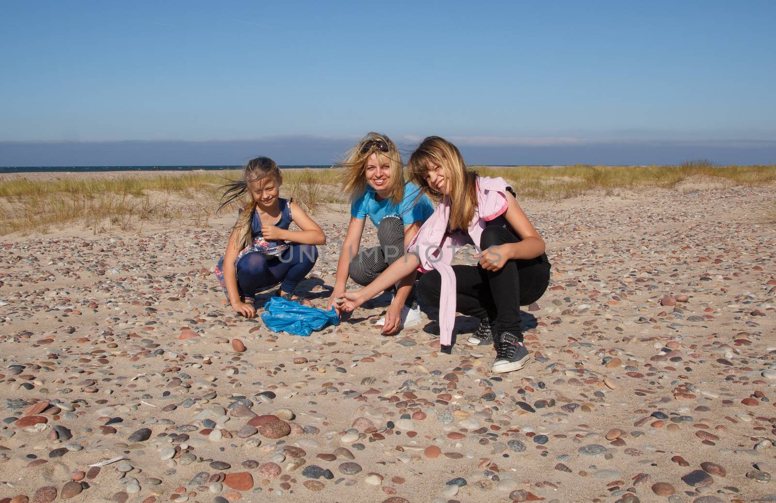 Three smiling girls on an empty beach collect stones