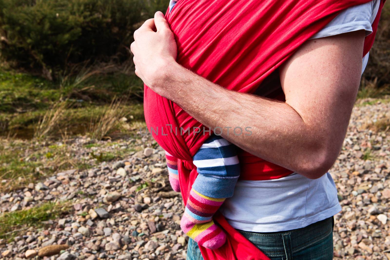Young father carrying abbay girl in a carrier sling