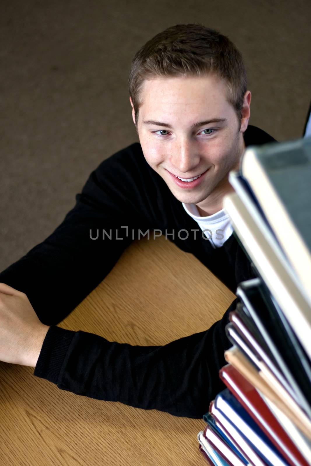 A student happily looks up at the high pile of textbooks he has to go through to do his homework assignment.