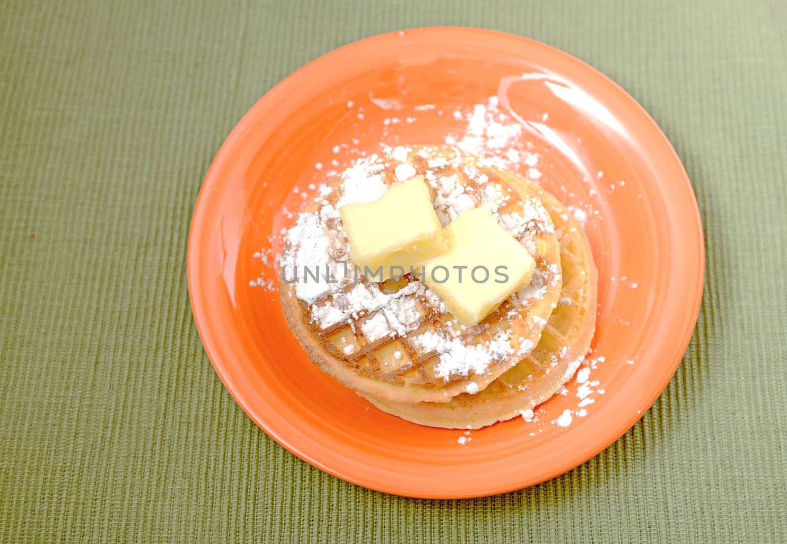 waffles with powdered sugar and butter on orange plate