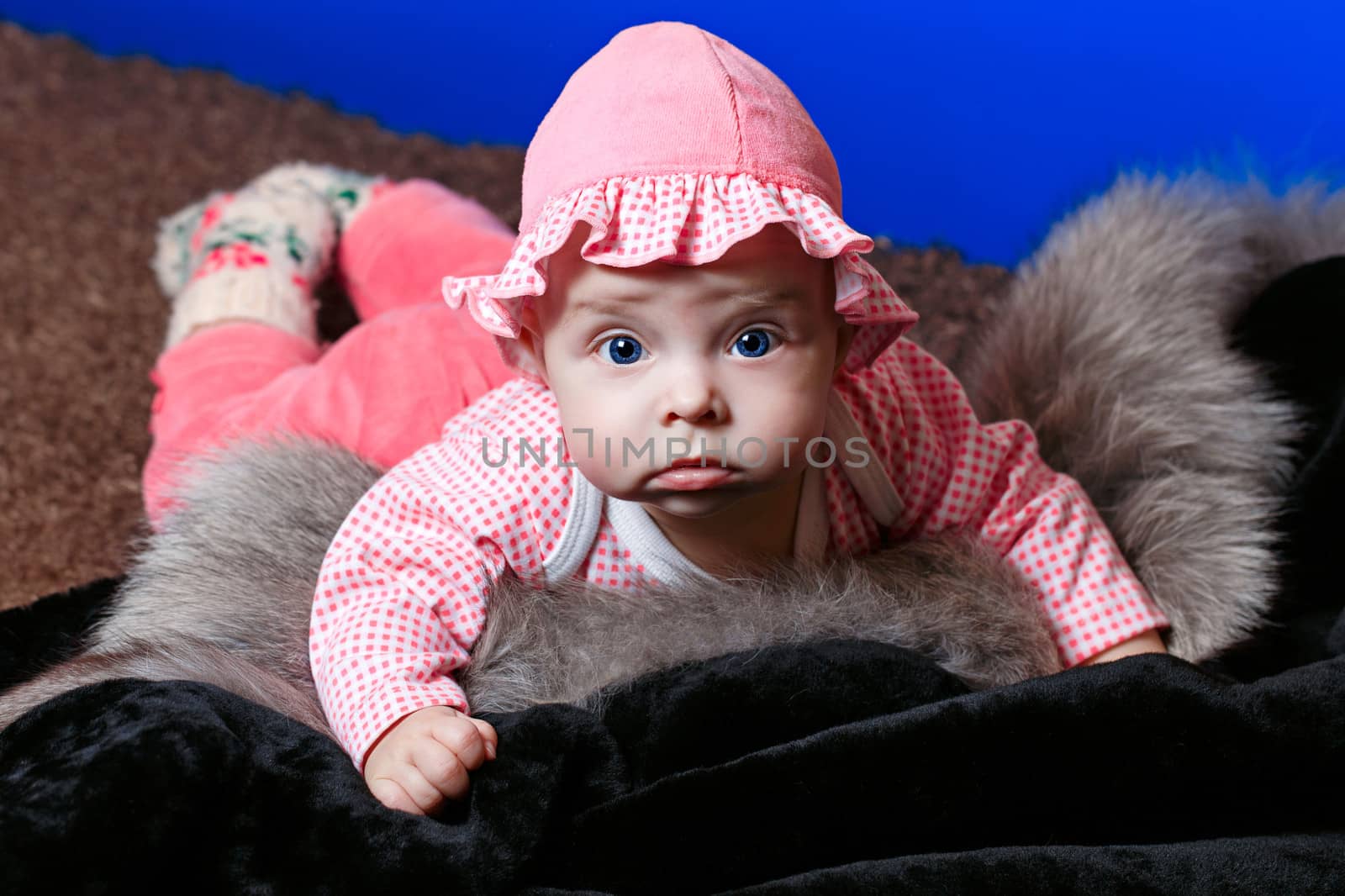 Baby with blue eyes lying on fur and looking at the camera