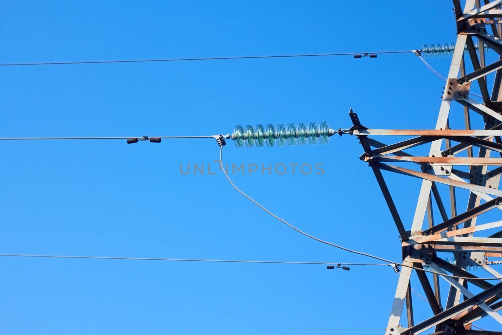 Insulators, wires, and fragment of metal electrical tower on the background of blue sky