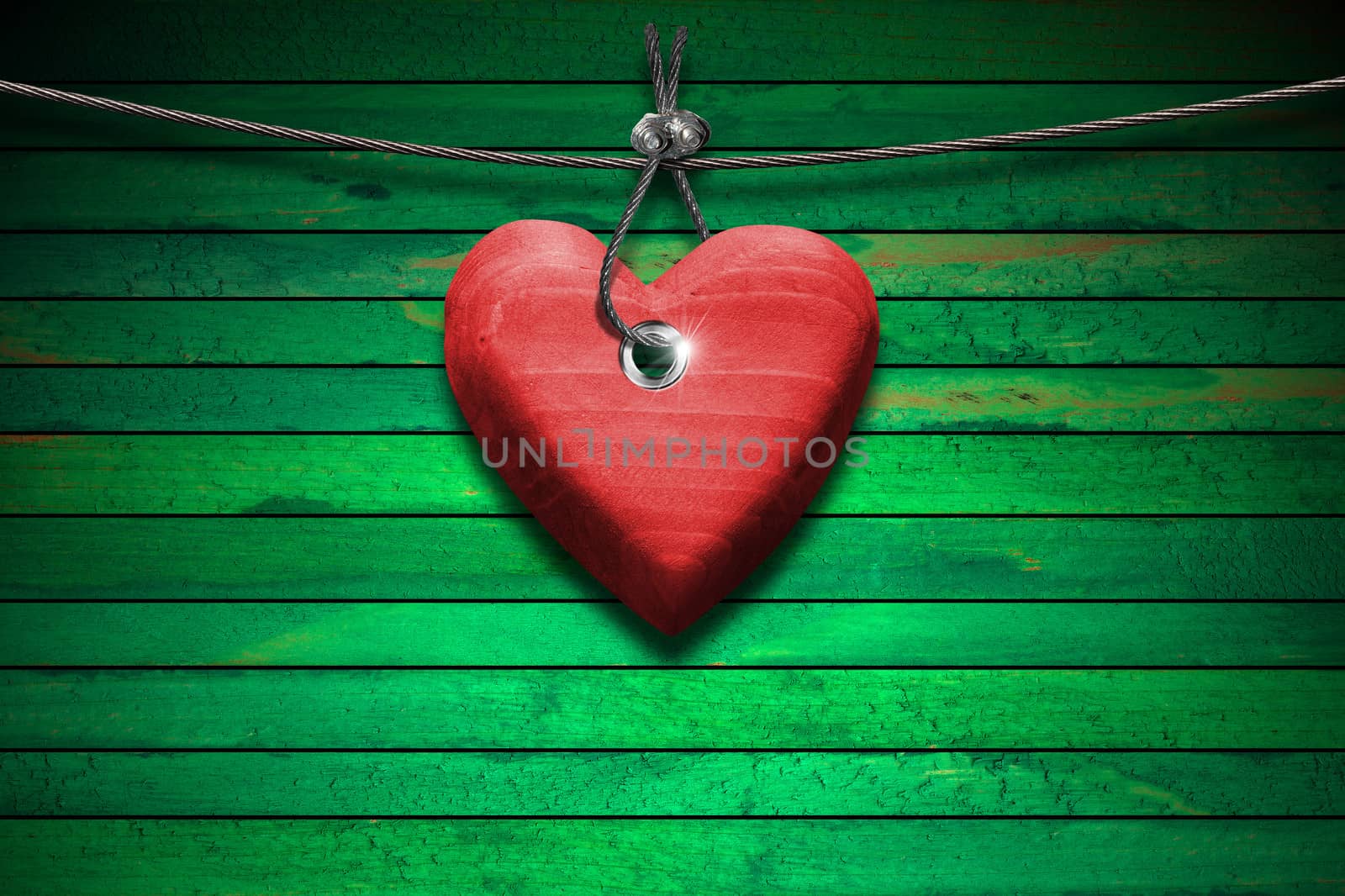 Handmade red wooden heart hanging on a steel cable on green wooden background