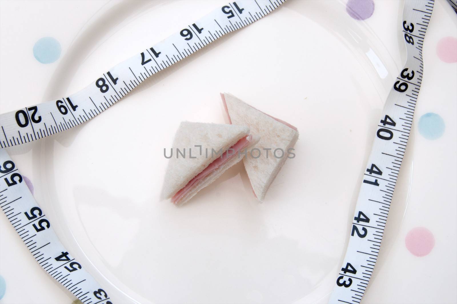 Bite size ham sandwich on a plate with a tape measure 