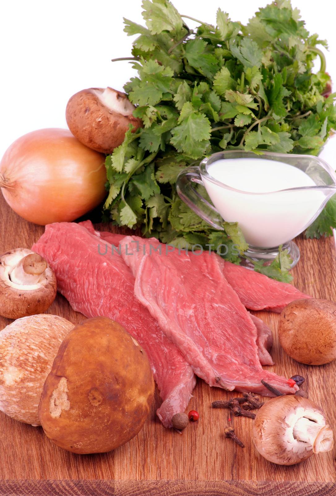 Cooking Beef Stroganoff. Arrangement of Ingredients with Raw Beef, Fresh Porcini Mushrooms, Onion, Spices, Greens and Milk closeup on Wooden Cutting Board