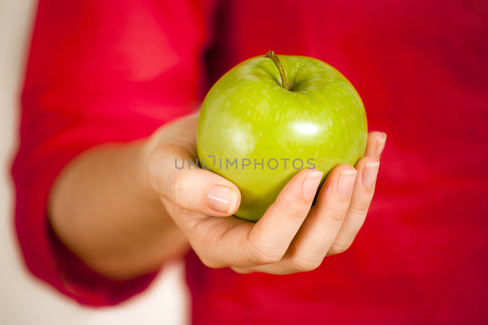 Photo of a woman's hand holding or giving a green apple. Shallow depth of field.
