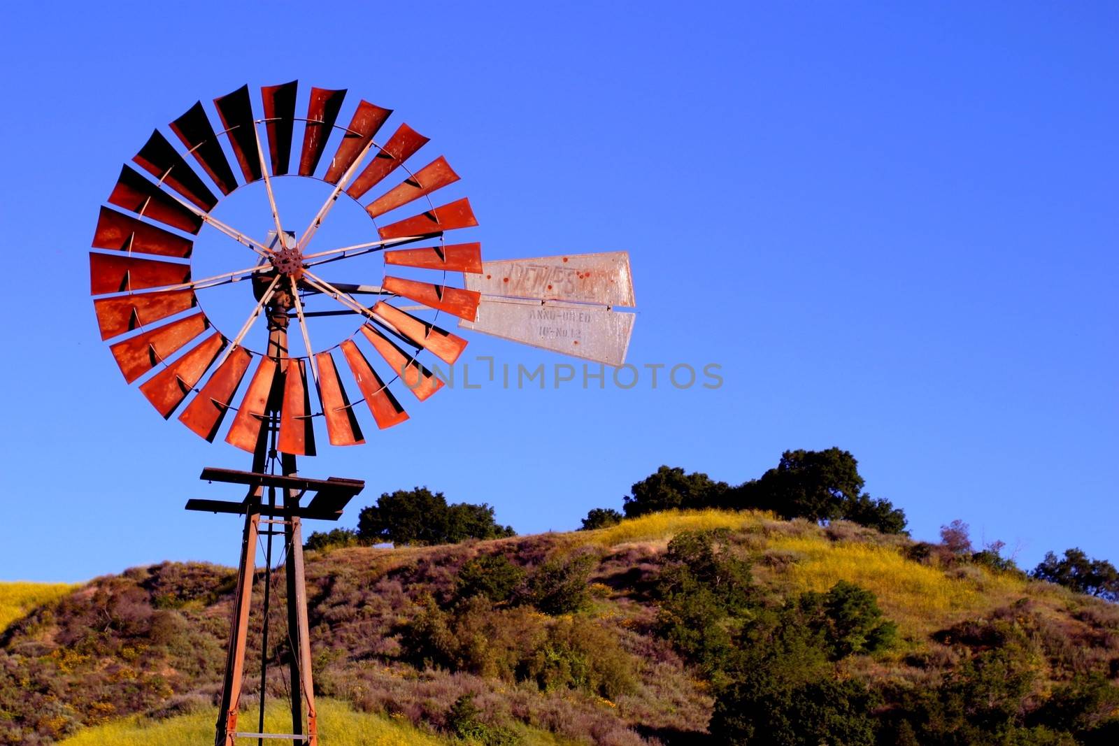 Water pumping windmill with a hill and blue sky in the background.