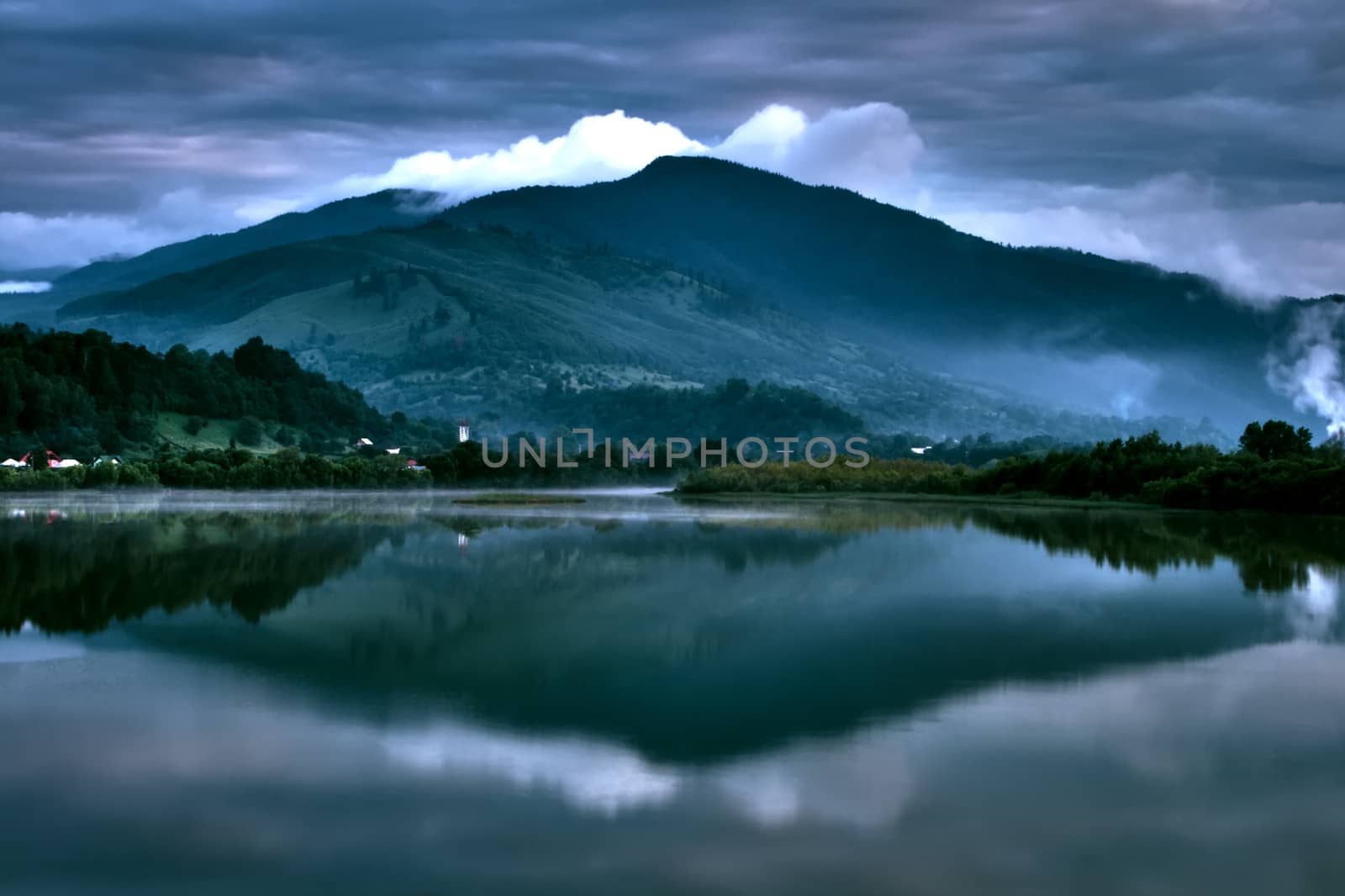 Beautiful blue reflection of the mountains in a perfectly still section of the lake below on a dark cloudy weather.